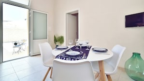 Un coin repas avec une table dressée pour quatre personnes, des chaises blanches et une porte vitrée donnant sur l’extérieur.
