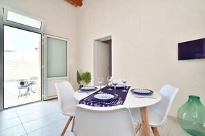 Een eetruimte met een tafel voor vier personen, witte stoelen en een glazen deur naar buiten.