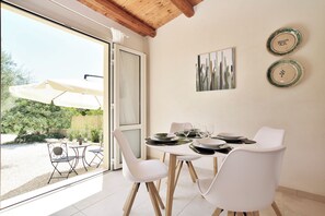 Un comedor con una mesa dispuesta para cuatro personas, sillas blancas y vista al jardín a través de un ventanal.