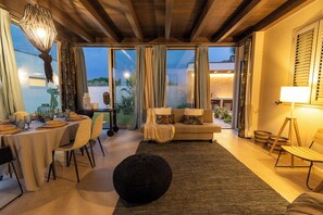 A dining area with a round table set for four, a sofa with cushions, and a black ottoman in the center. - Villa Olive & Champagne con Piscina Privata (Ispica)