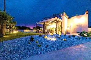 A modern house with a covered outdoor area, a garden with blue pebbles, and a well-lit entrance. - Villa Olive & Champagne con Piscina Privata (Ispica)