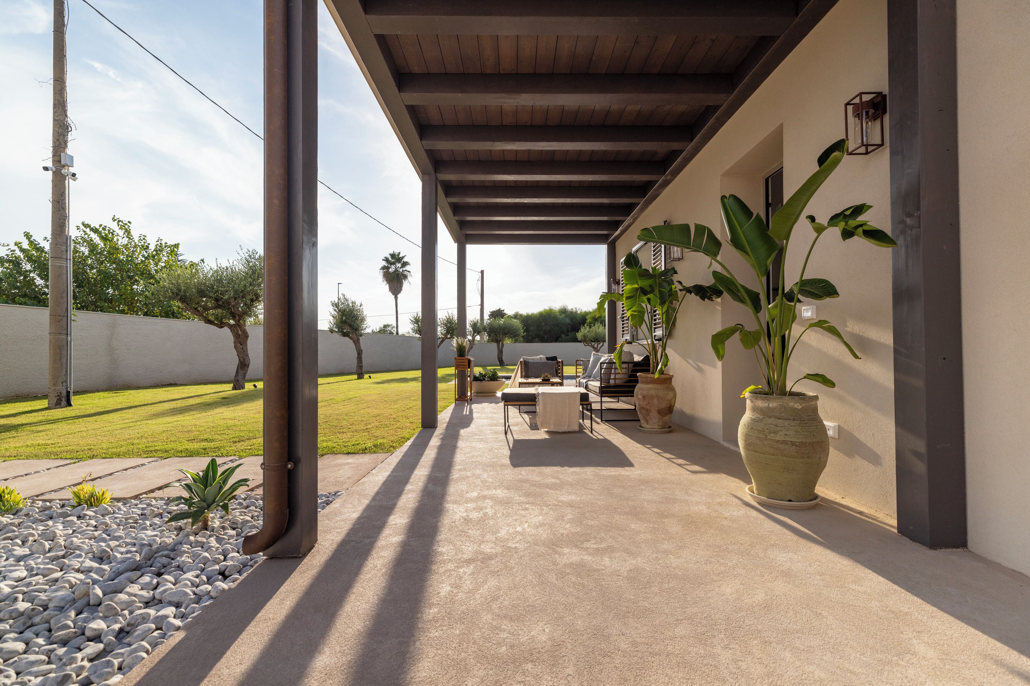 A covered patio area with a concrete floor, outdoor furniture, and potted plants.