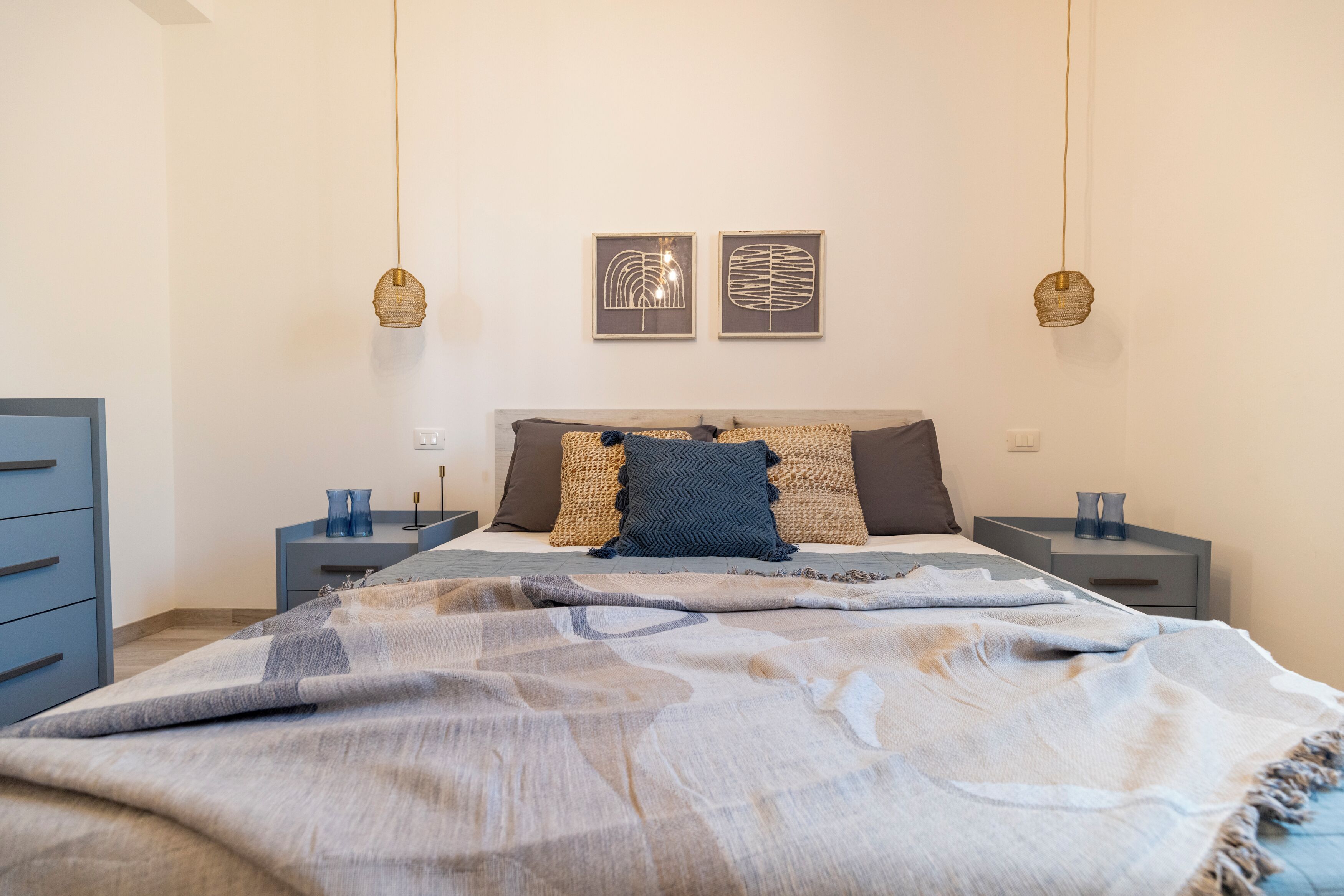 Un dormitorio con una cama, dos mesitas de noche, un aparador y decoración en la pared.