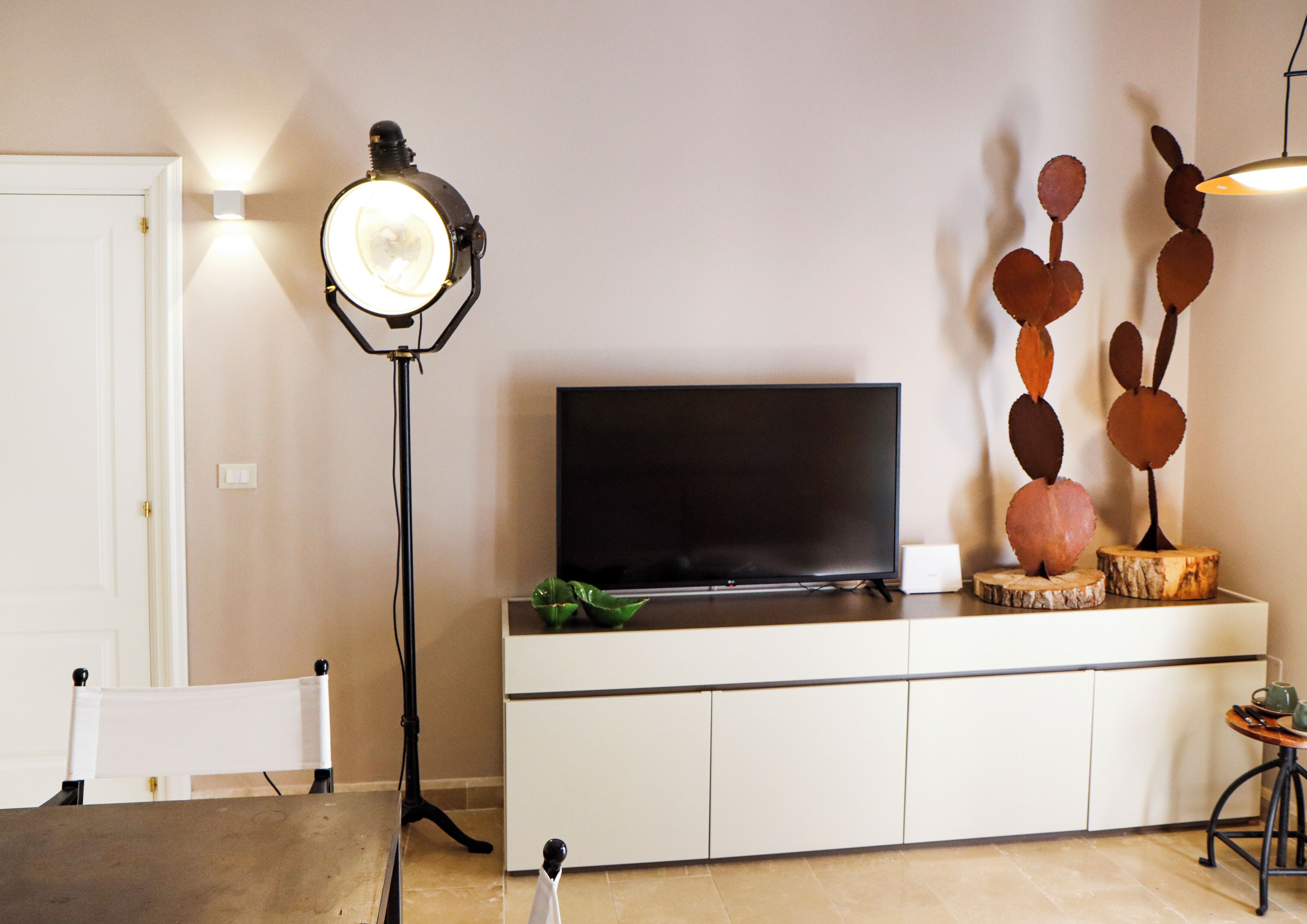 Una sala de estar moderna con un televisor de pantalla plana sobre un mueble blanco, una lámpara de pie y un elemento decorativo en la pared.