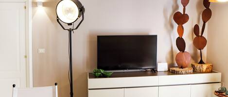 Una sala de estar moderna con un televisor de pantalla plana sobre un mueble blanco, una lámpara de pie y un elemento decorativo en la pared.
