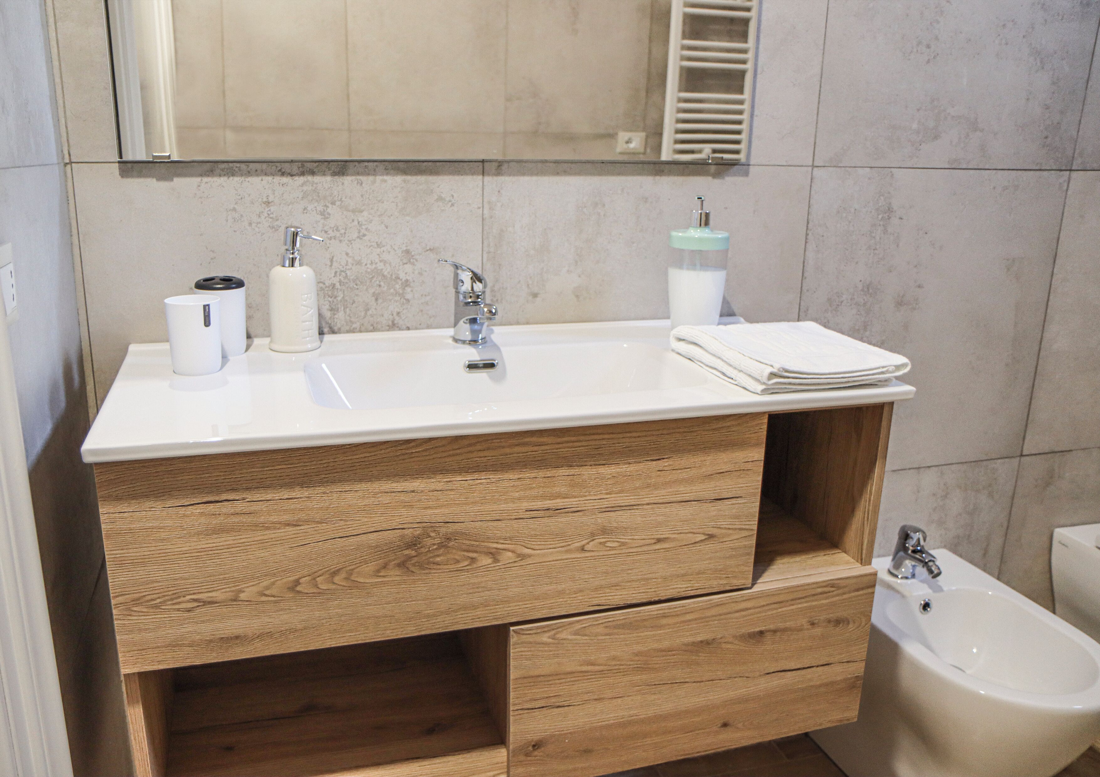 Un baño moderno con lavamanos blanco, tocador de madera y un bidé.