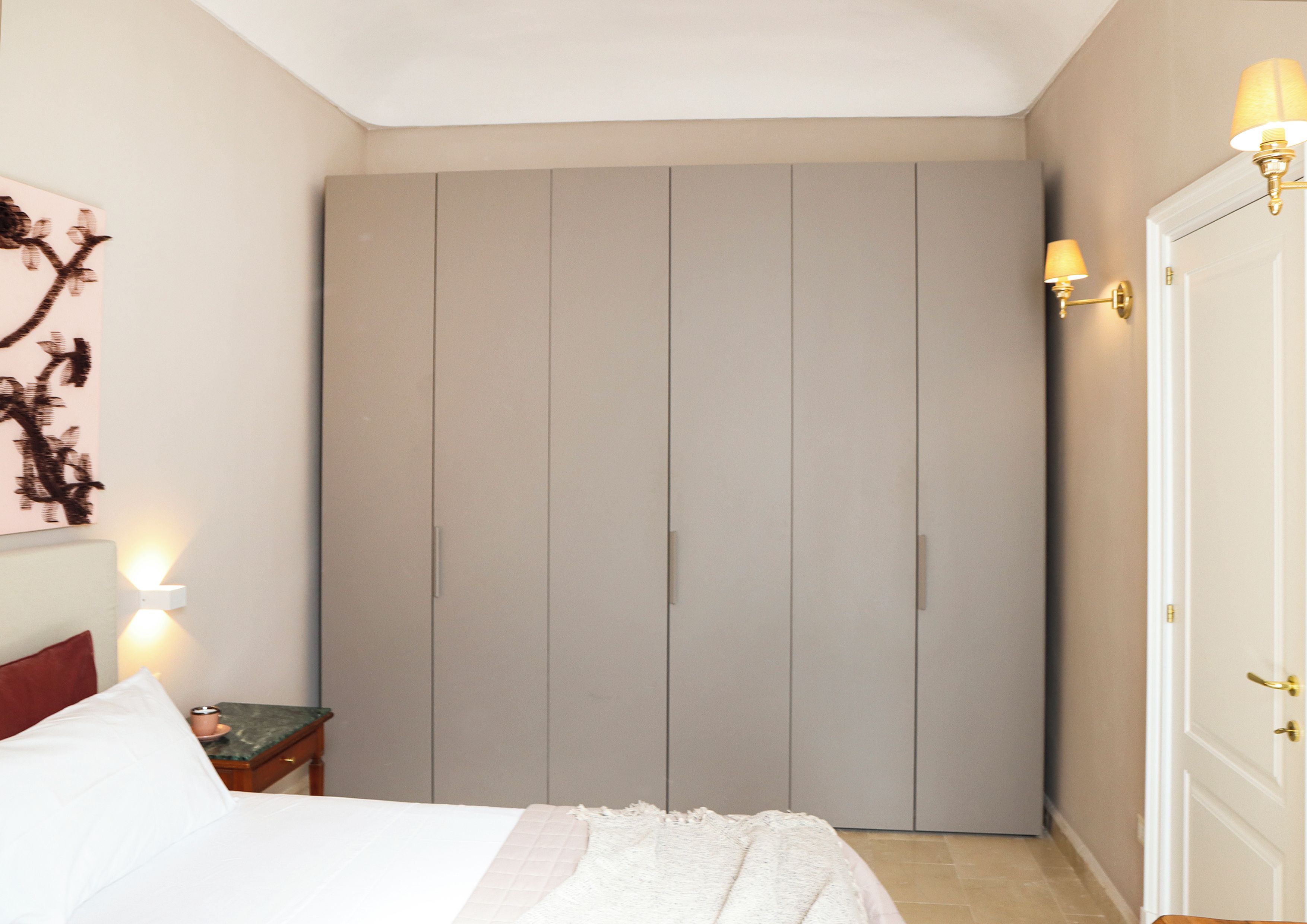 A bedroom with a bed, a nightstand, a wardrobe, and wall sconces.