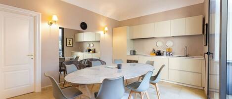 A modern kitchen with a round dining table, grey chairs, and light-colored cabinets.