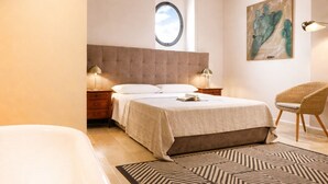 Ein Schlafzimmer mit einem großen Bett, einem runden Fenster, einem Sessel und einem Bild an der Wand.