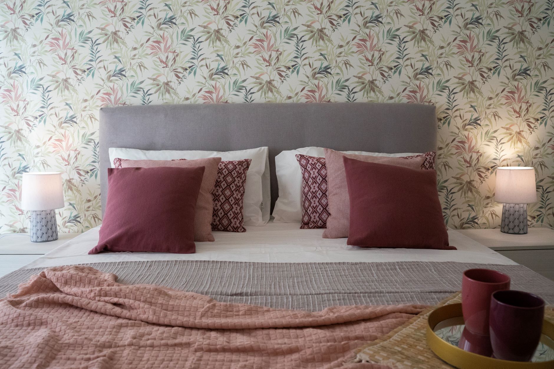Un lit bien fait, avec une tête de lit grise, plusieurs oreillers et une couverture rose.