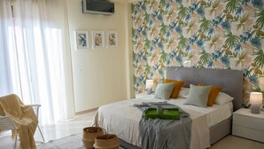 Un dormitorio con cama, mesitas de noche, una silla y una pared con estampado de hojas tropicales.