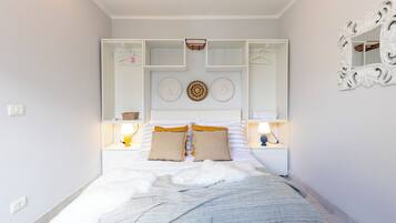 A bedroom with a bed, a white wardrobe, a mirror, and a bedside table with a lamp.