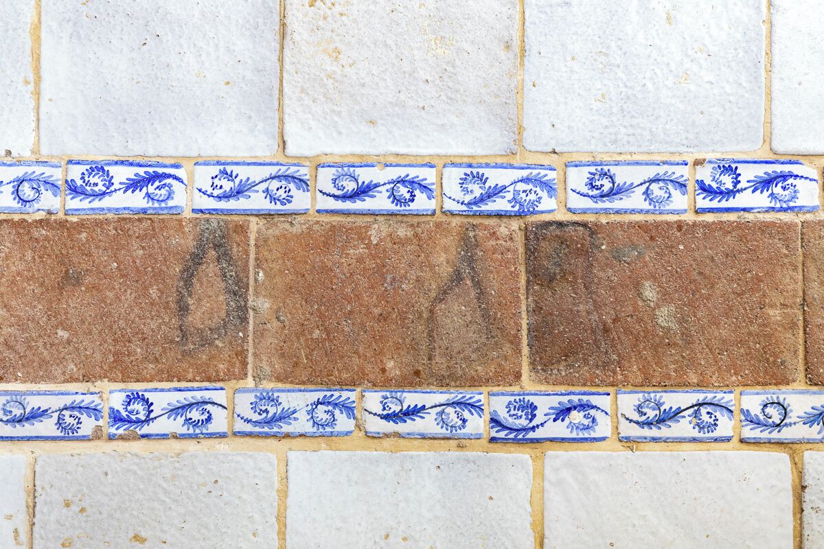 A section of a tiled wall with alternating white and brown tiles, featuring blue floral patterns along the edges.