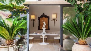 Un comedor con una mesa blanca, sillas y una estatua como centro de mesa. Hay dos lámparas fijadas a la pared y un espejo grande sobre la mesa.