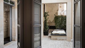 Un couloir étroit, avec un lit et une plante en pot, qui mène à un mur de pierre.