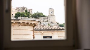 Une vue d’un bâtiment historique doté d’une tour horlogée, d’un mur fortifié et d’une église en arrière-plan.