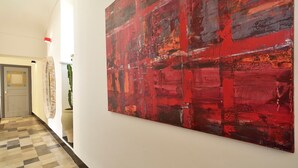 A hallway with a large abstract red painting on the wall, a patterned floor, and a door with a glass panel. - Domus Sbirciò Modica (Modica)