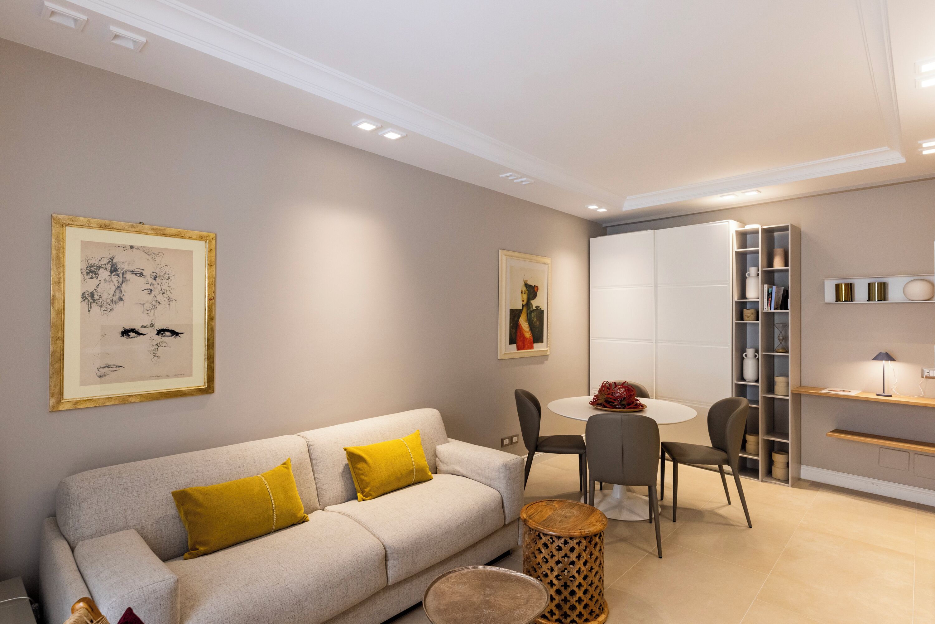 A modern living room with a sofa, chairs, a round table, and a bookshelf.