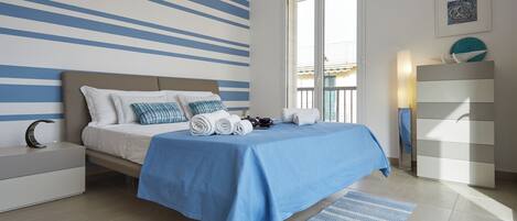 Ein modernes Schlafzimmer mit Bett, Nachttisch, Kommode und Blick auf den Balkon.