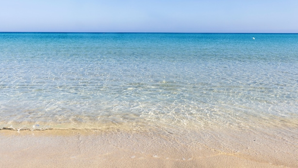 Una vista despejada d'una platja amb aigua tranquil·la i sorra daurada.