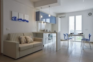 Una sala de estar moderna con sofá, una zona de comedor con sillas, una isla de cocina y obras de arte en la pared.