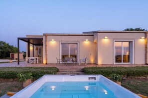 Ein modernes Haus mit Swimmingpool, Sitzgelegenheiten im Freien und großen Fenstern.