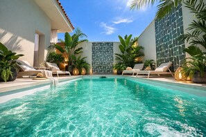 A swimming pool with lounge chairs, surrounded by tropical plants and a stone wall. - Villa Aman Piscina e Jacuzzi Riscaldata (Ispica)