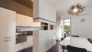 Una cocina moderna con armarios blancos, horno empotrado y comedor con mesa y sillas blancas.