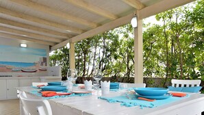 Un área de comedor al aire libre con una mesa blanca dispuesta para cuatro personas, rodeada de árboles.