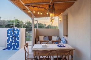 A covered outdoor seating area with a table and chairs, a woven ceiling, and a view of greenery. - Blue Riad (Ispica)