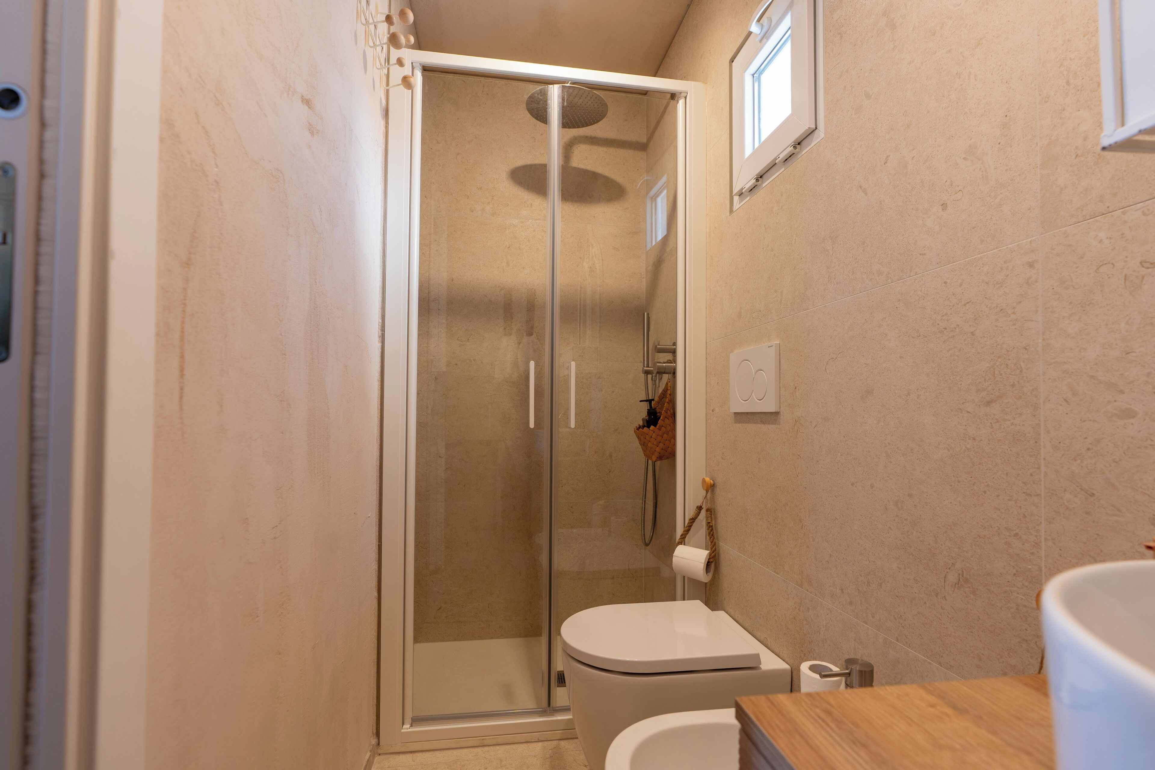 Une salle de bain avec une douche à parois de verre, des toilettes blanches et un plan de toilette en bois.