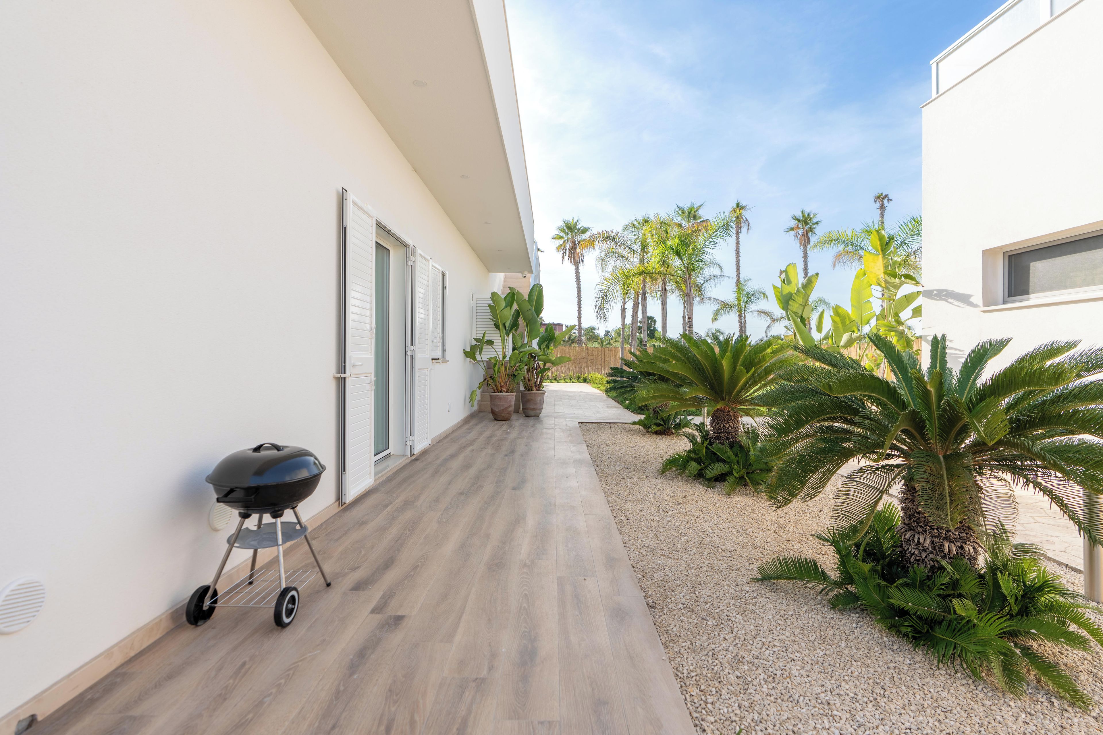 Un bâtiment moderne doté d’un plancher en bois, d’un barbecue et de plantes tropicales.