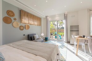 A modern bedroom with a large bed, a dining area with a table and chairs, and a view of a garden through a sliding glass door. - Perla del Mare (Ispica)