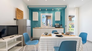 Una cocina moderna con una pared de acento color aguamarina, una zona de comedor con sillas azules y un televisor sobre una mesa blanca.