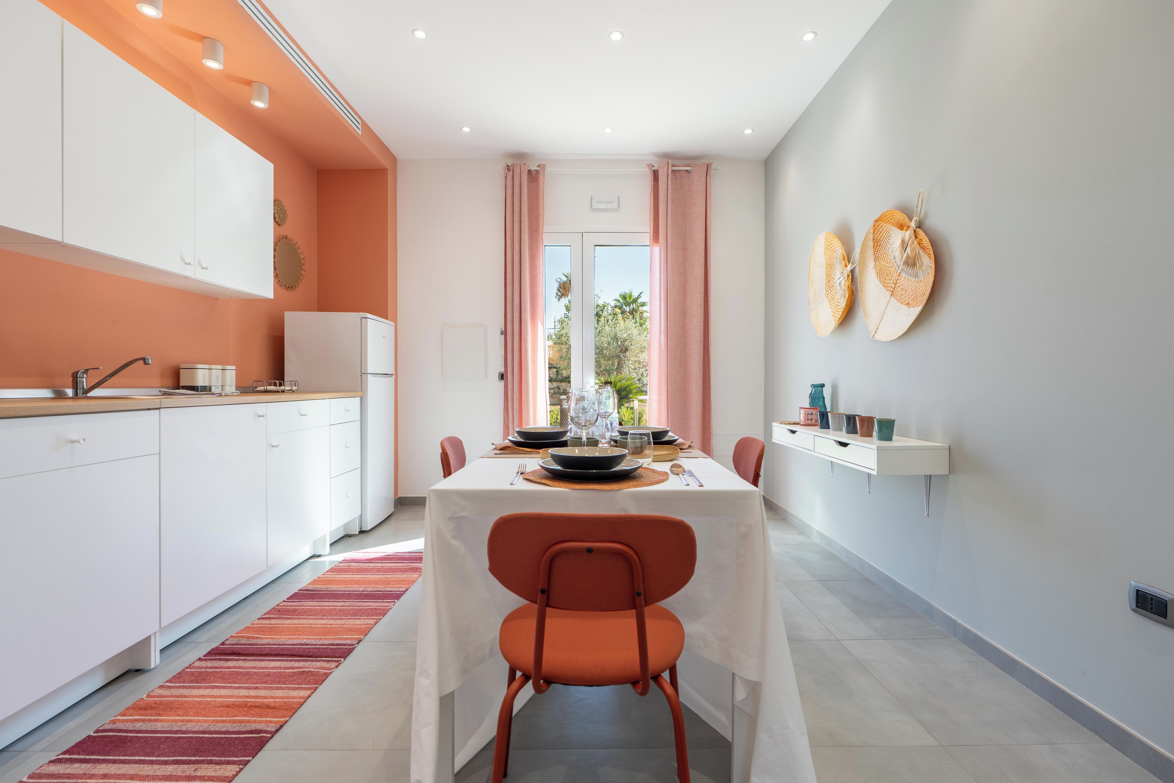 A modern kitchen with white cabinets, a dining table set for four, and a view through a glass door to the outdoors.