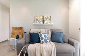 A modern living room with a grey sofa, blue and white patterned pillows, and a wall-mounted shelf with two framed artworks. - Perla del Mare (Ispica)