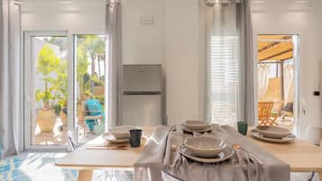 A dining area with a table set for four, a refrigerator, and a view of the garden through glass doors.