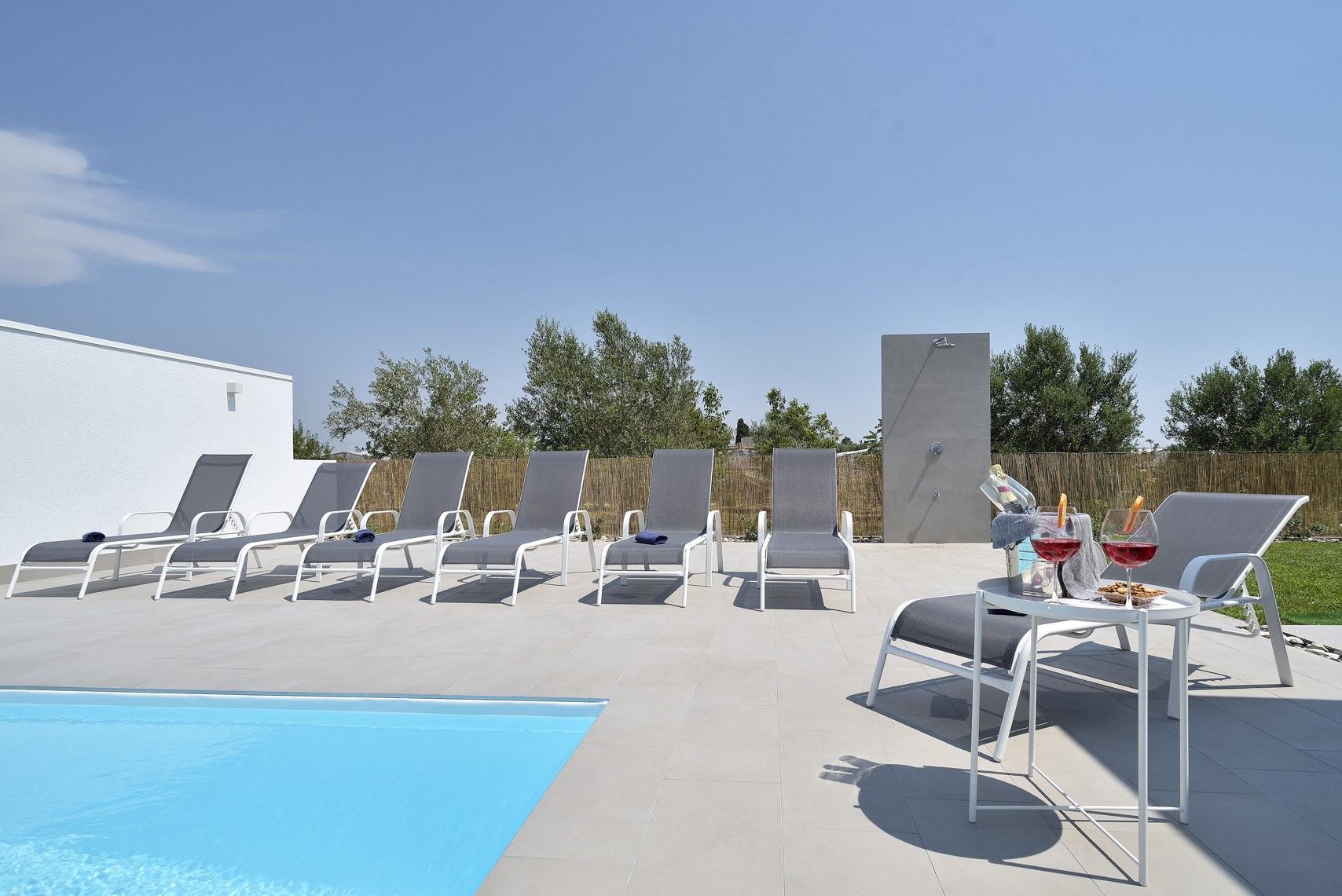 Zona de piscina con sillones de descanso, una pequeña mesa con bebidas y una ducha.