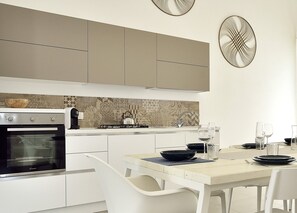 A modern kitchen with white cabinets, a gas stove, and a dining area with a table set for two. - Villa Giaira Sicilymyhome (Ispica)