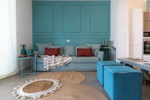 A modern living room with a teal accent wall, a grey sofa with red cushions, and a blue ottoman. - Villa Giaira Sicilymyhome (Ispica)