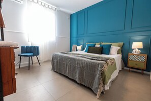 A bedroom with a bed, a blue chair, a bedside table, and a dresser. - Villa Giaira Sicilymyhome (Ispica)