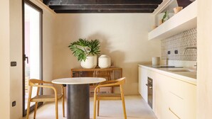 Een kleine keuken met een ronde tafel, twee stoelen, een potplant en een inbouwoven.