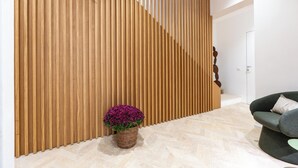 Un interior moderno con un panel de pared de listones de madera, una cesta de mimbre con flores moradas y un sofá verde oscuro.