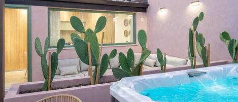 A modern outdoor area with a hot tub, cacti, and a seating area with cushions.