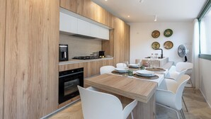 Una cocina moderna con armarios de madera, horno integrado y un comedor con mesa de madera y sillas blancas.