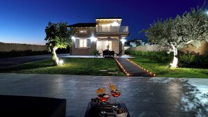 Une maison moderne à deux étages, dotée d’une allée bien éclairée, d’un espace extérieur aménagé et d’une petite piscine.