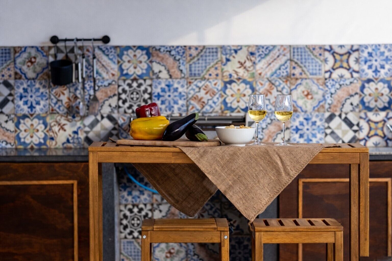 A wooden table with a cloth, a bowl of cereal, two glasses of white wine, and a red bell pepper.