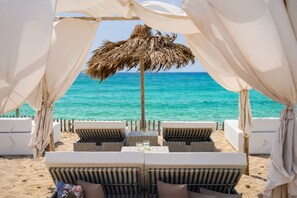 A beach cabana with a thatched roof, white curtains, and wicker lounge chairs facing the ocean. - Villa Emanto Sicilymyhome (Ispica)