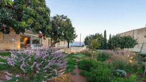 Un jardin avec un mur en pierre, un sentier et un bâtiment doté d’une terrasse.