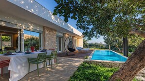 Un espace extérieur moderne aménagé pour les repas, avec une piscine, des murs en pierre et de la verdure.
